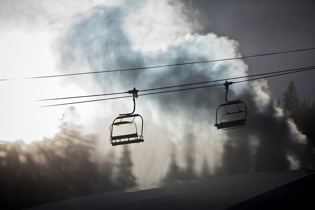 Silhouette of a chairlift on a ski hill with man made snow from  snow gun backlit by the sunlight, Copper Mountain Resort; Colorado, United States of America