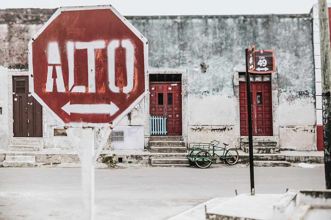 A stop sign with an arrow in Spanish along a street with houses in the background; Cancun, Mexico