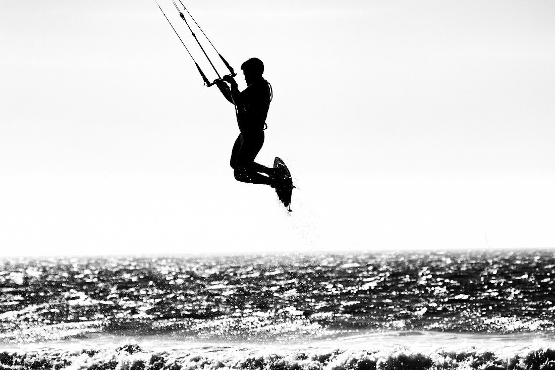 A silhouetted image of a kite surfer taking air over the Pacific Ocean in San Diego, California