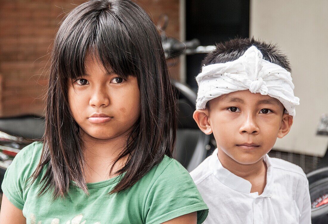 Balinese girl and boy watching a procession in Ubud, the island's cultural capital. The boy wears traditional costume. Bali, Indonesia.