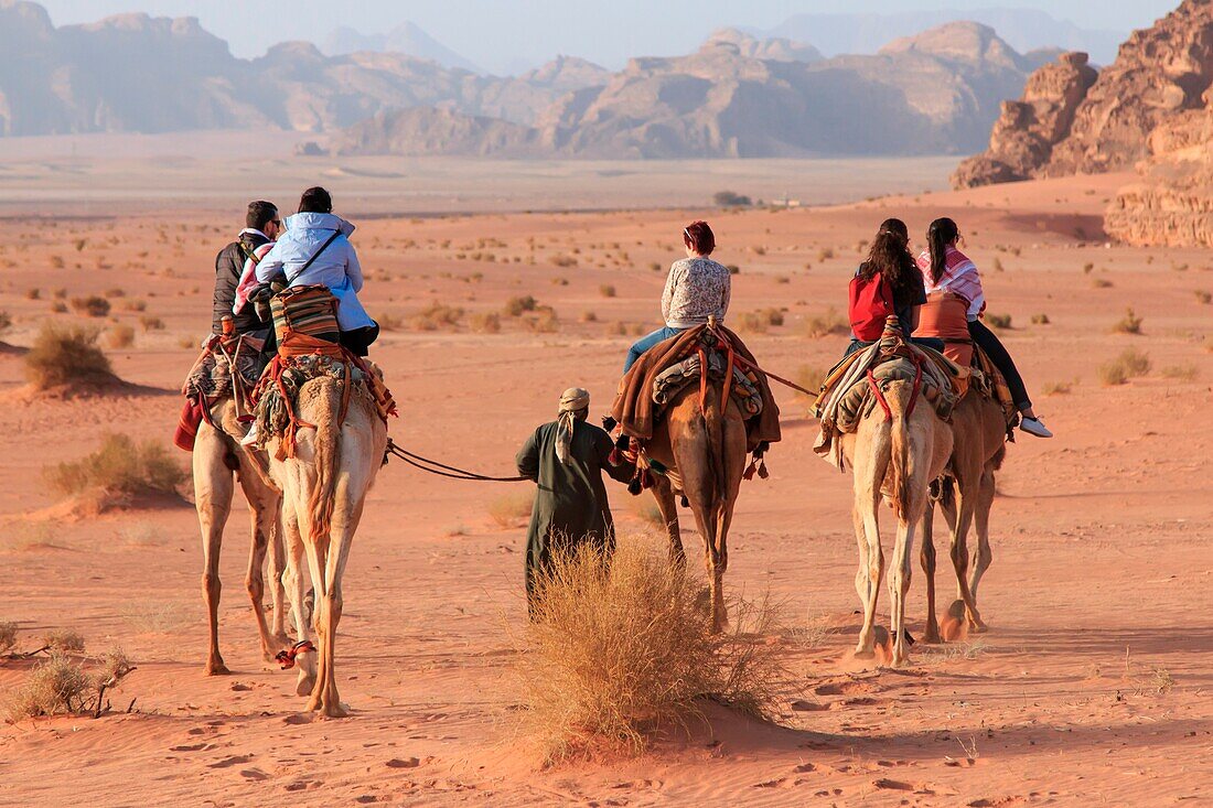 Tourists riding camels at sunset in the Wadi Rum desert, Jordan.