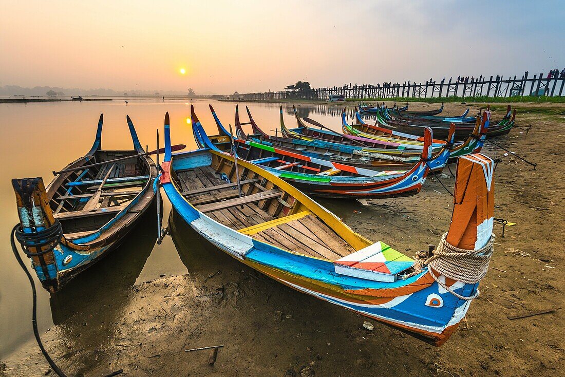 Amarapura, Mandalay region, Myanmar. Colorful boats moored on the banks of the Taungthaman lake at sunrise, with the U Bein bridge in the background.