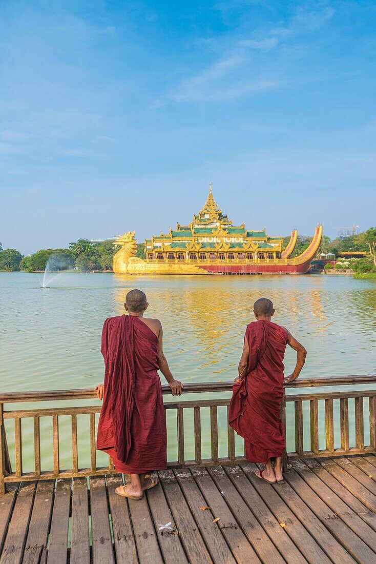 Yangon, Myanmar (Burma). Two monks watching the Karaweik Palace on the Kandawgyi Lake.