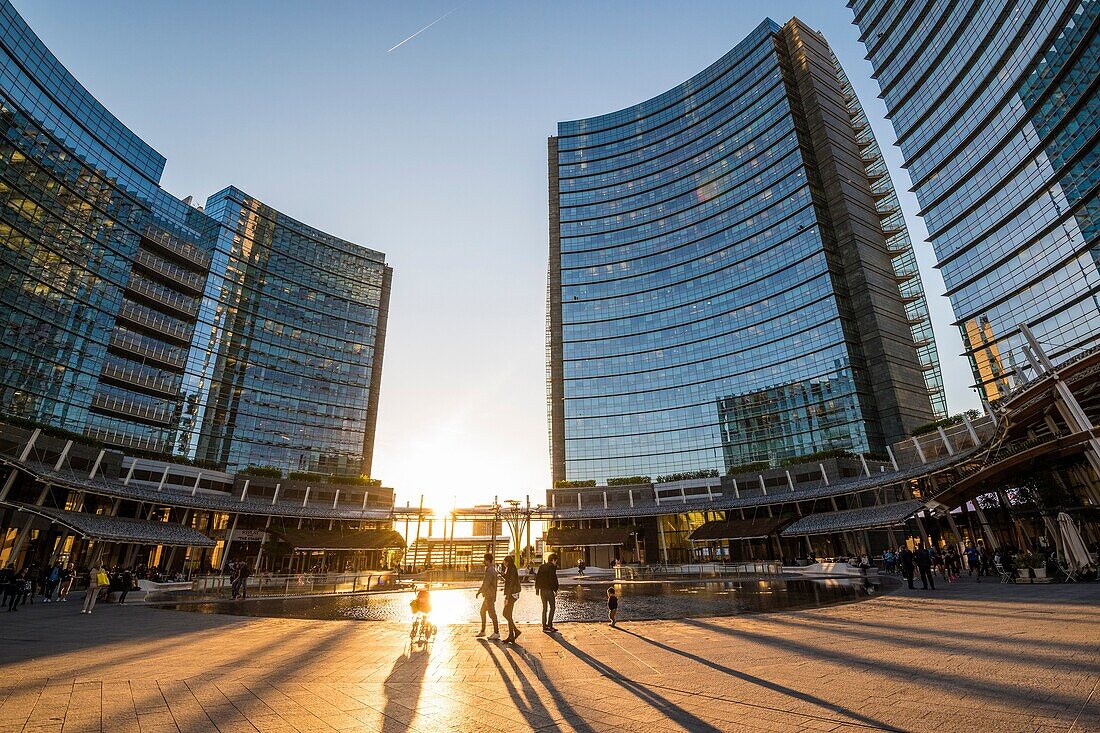 Milan, Lombardy, Italy. People walking in Gae Aulenti square in the Porta Nuova business district at sunset.