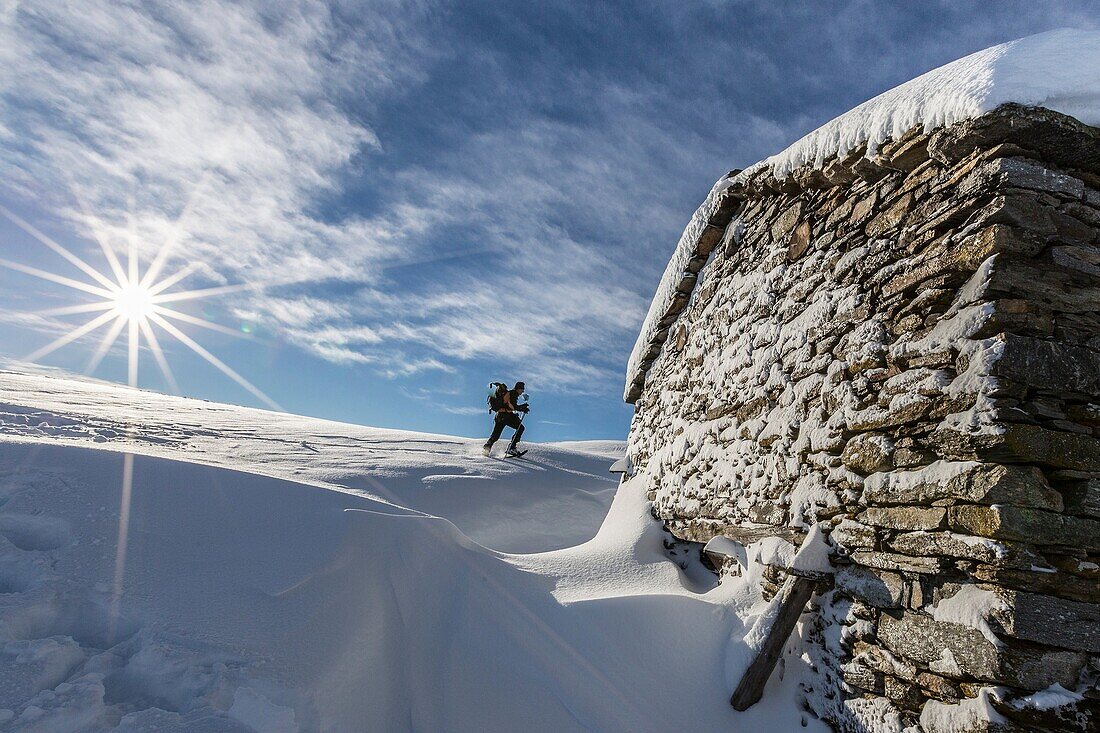 Snowshoe hiker walking near snow covered hut Motta di Olano Gerola Valley Valtellina Orobie Alps Lombardy Italy Europe.