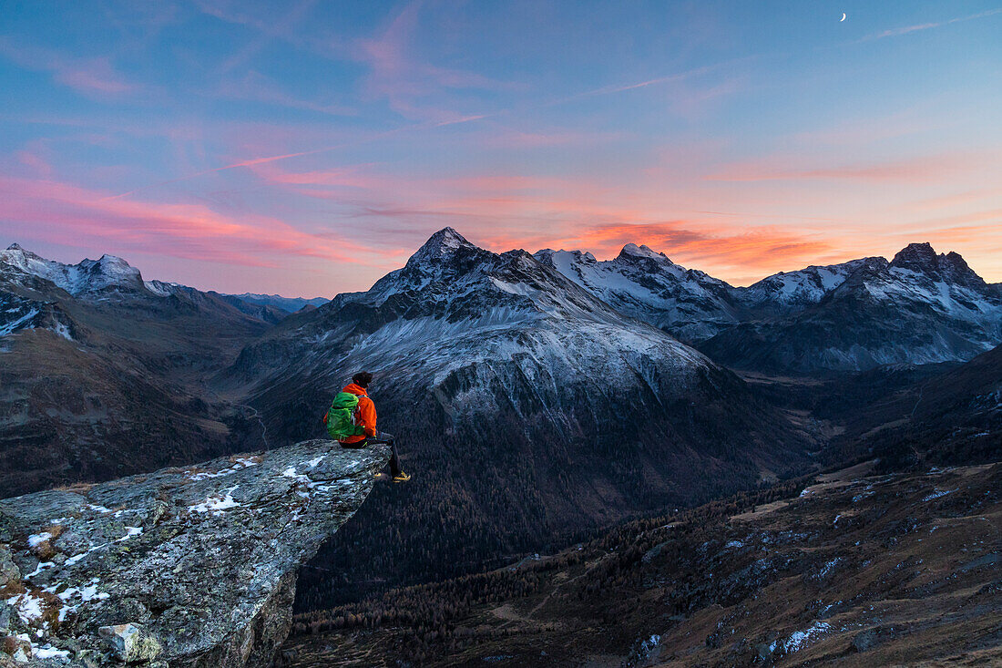 An hiker on a rock in Viola valley with a panoramic view at sunset, Valdidentro, Valtellina, Lombardy, Italy