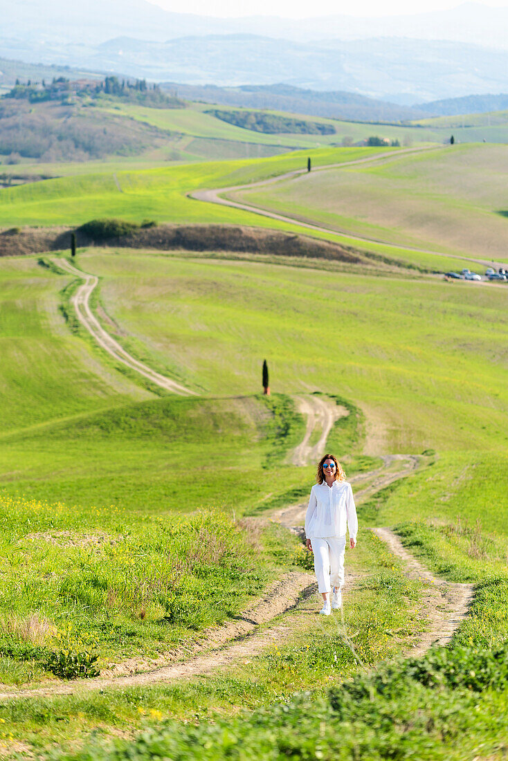 San Quirico d'Orcia, Orcia valley, Siena, Tuscany, Italy. A young woman in casual clothes is walking along a country road