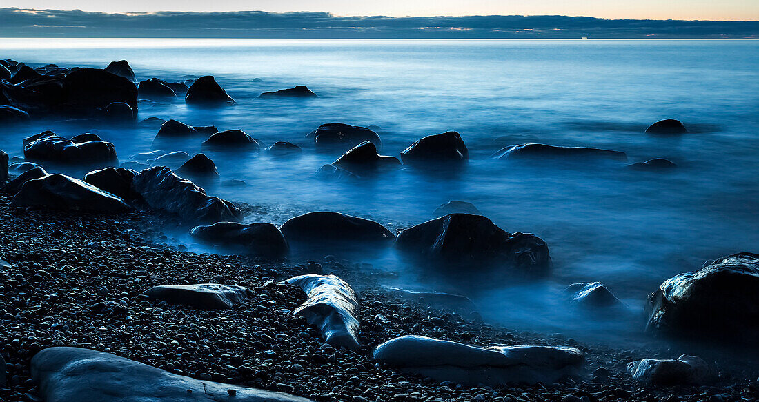 Beautiful blue misty ocean washing in against rocks on a West Coast beach; Greymouth, New Zealand