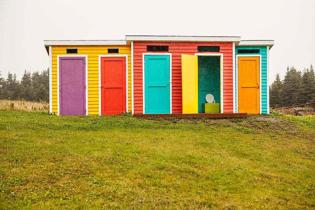 Colourful buildings for bathrooms and change rooms with multi-coloured siding and doors on grass; Newfoundland, Canada