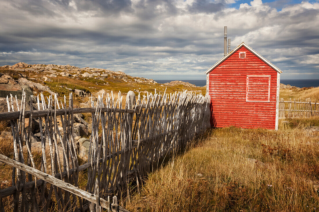 A small red shed beside a wooden picket fence along the coast; Newfoundland, Canada