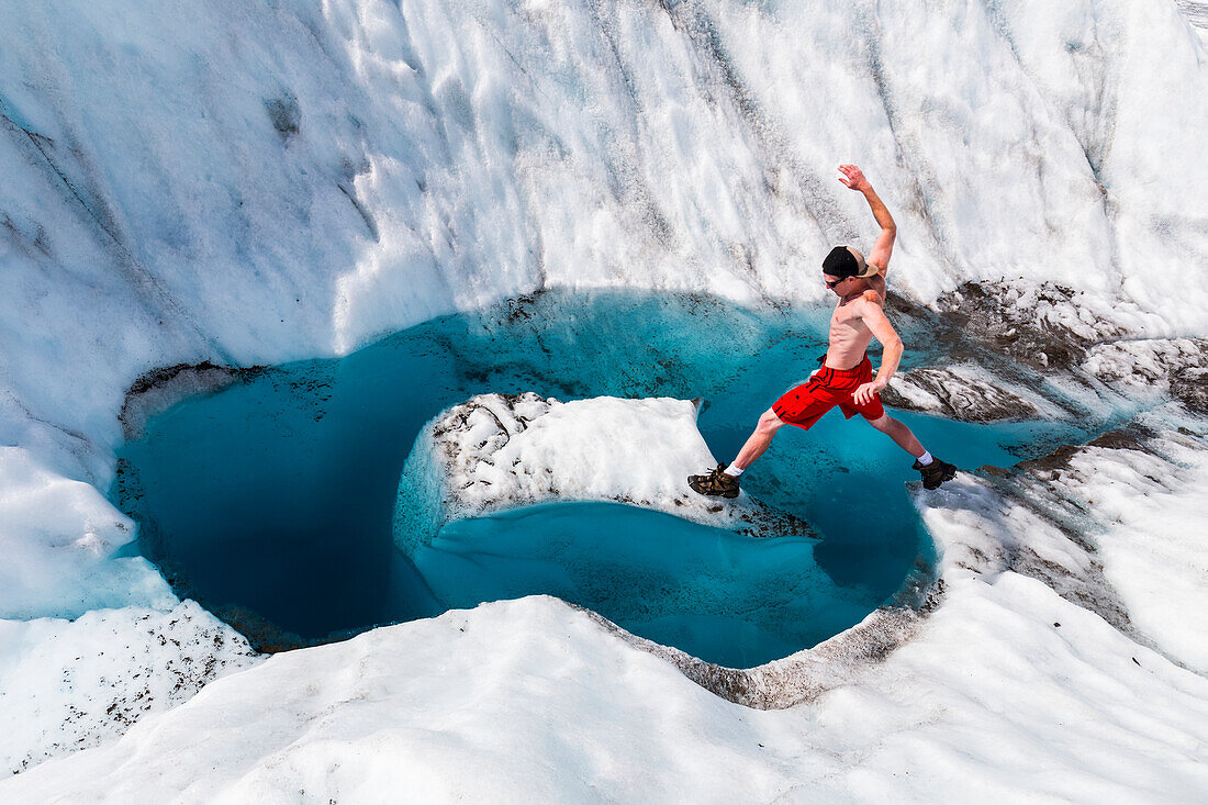 A man jumps onto an island of ice on Root Glacier in Wrangell-St. Elias National Park; Alaska, United States of America