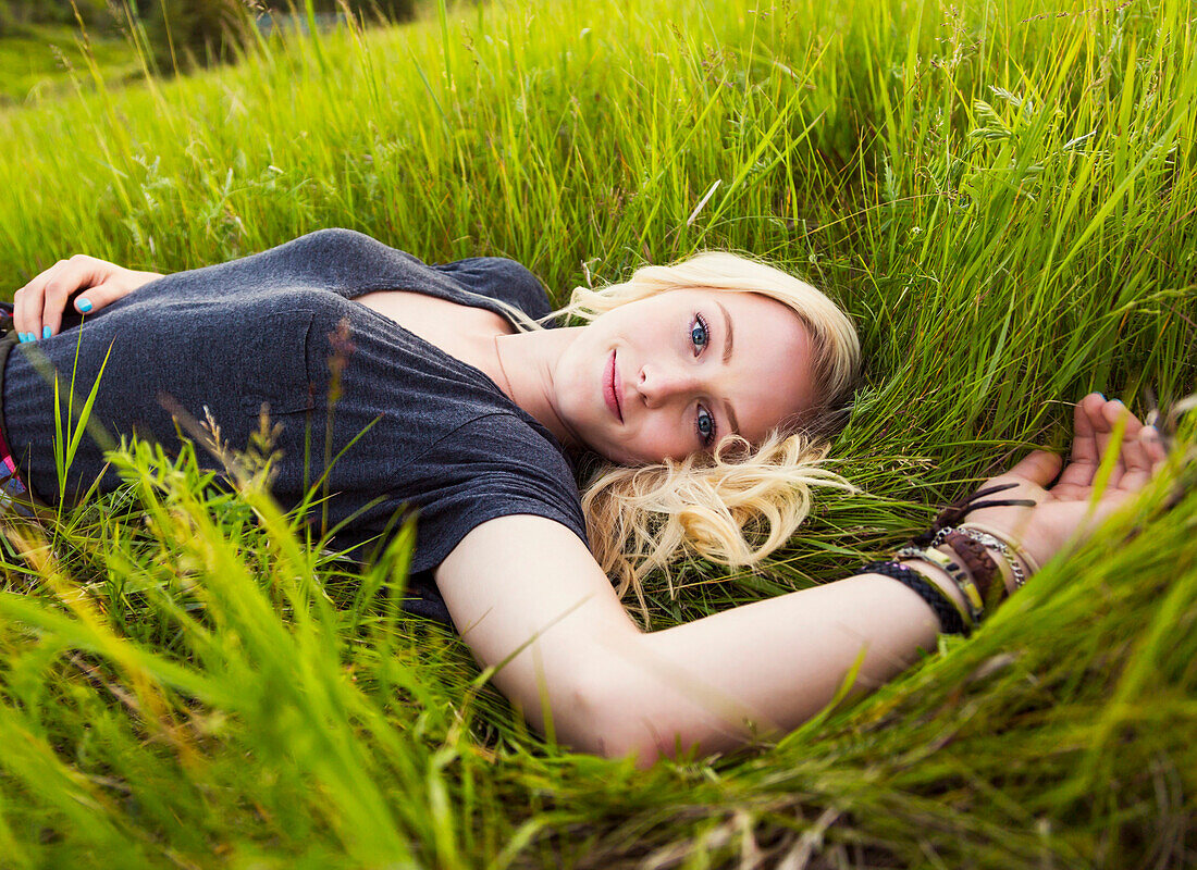 Porträt einer jungen Frau mit langen blonden Haaren, die in einem Park im Gras liegt; Edmonton, Alberta, Kanada