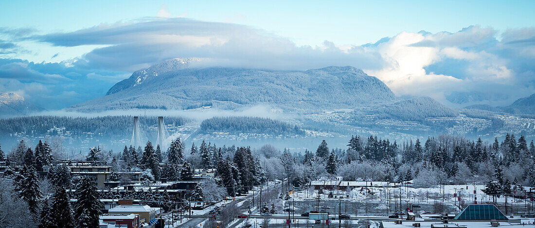 View of clouds hovering over mountains and snow covering the neighbourhood in the foreground; Surrey, British Columbia, Canada