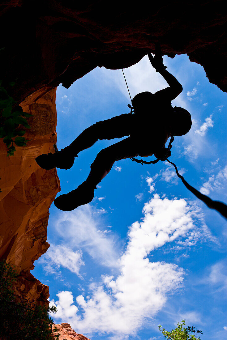 Looking upwards to the silhouette of an adventurer rappelling down a canyon in the desert; Hanksville, Utah, United States of America