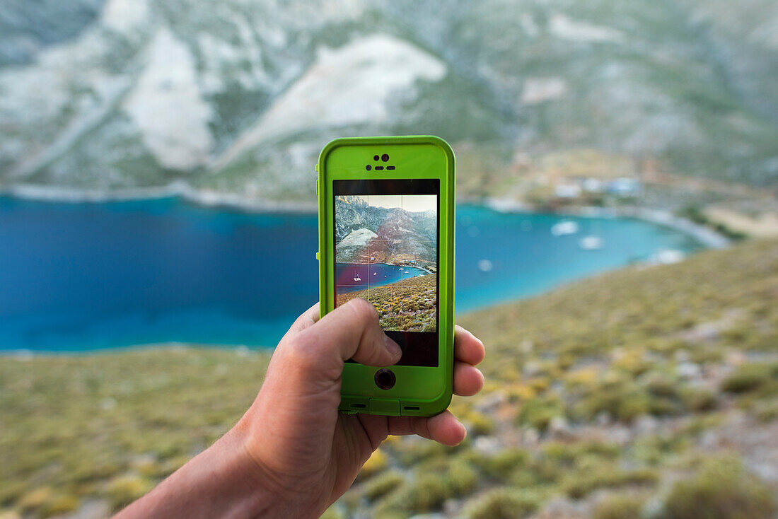 Personal perspective shot of person taking picture with smartphone of coastline and sea, Kalymnos, Greece