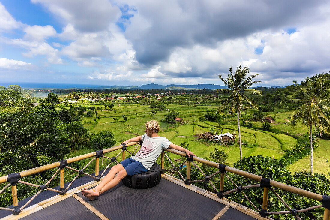 Clouds over young man relaxing alone on tree house balcony, Bali, Indonesia