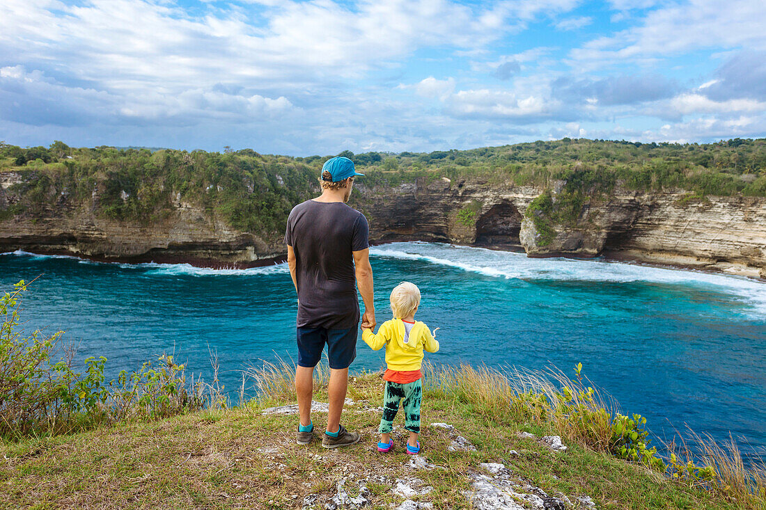 Father and son standing on edge of coastal cliff and admiring ocean, Bali, Indonesia