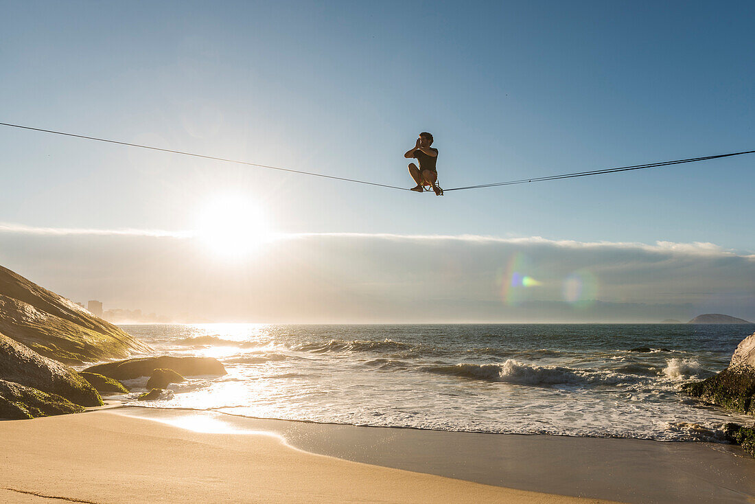 Man slacklining and waterlining during sunrise above Leblon Beach, Rio de Janeiro, Brazil