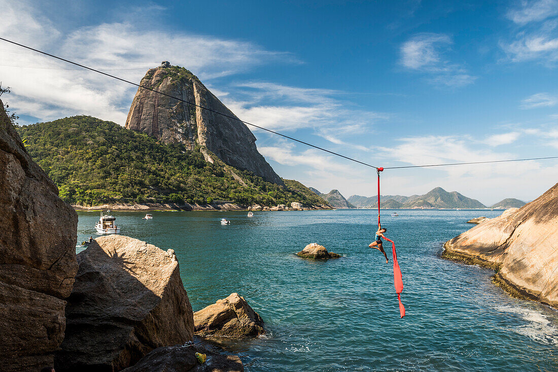 Woman doing aerial acrobatics hanging from highline next to Sugarloaf Mountain in Rio de Janeiro, Brazil