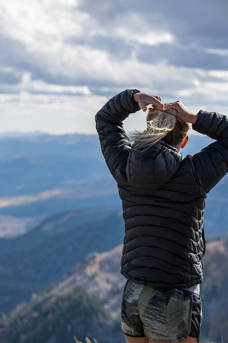 Woman preparing for outdoor adventure by securing ponytail while looking at mountain view, Jackson Hole, Wyoming, USA