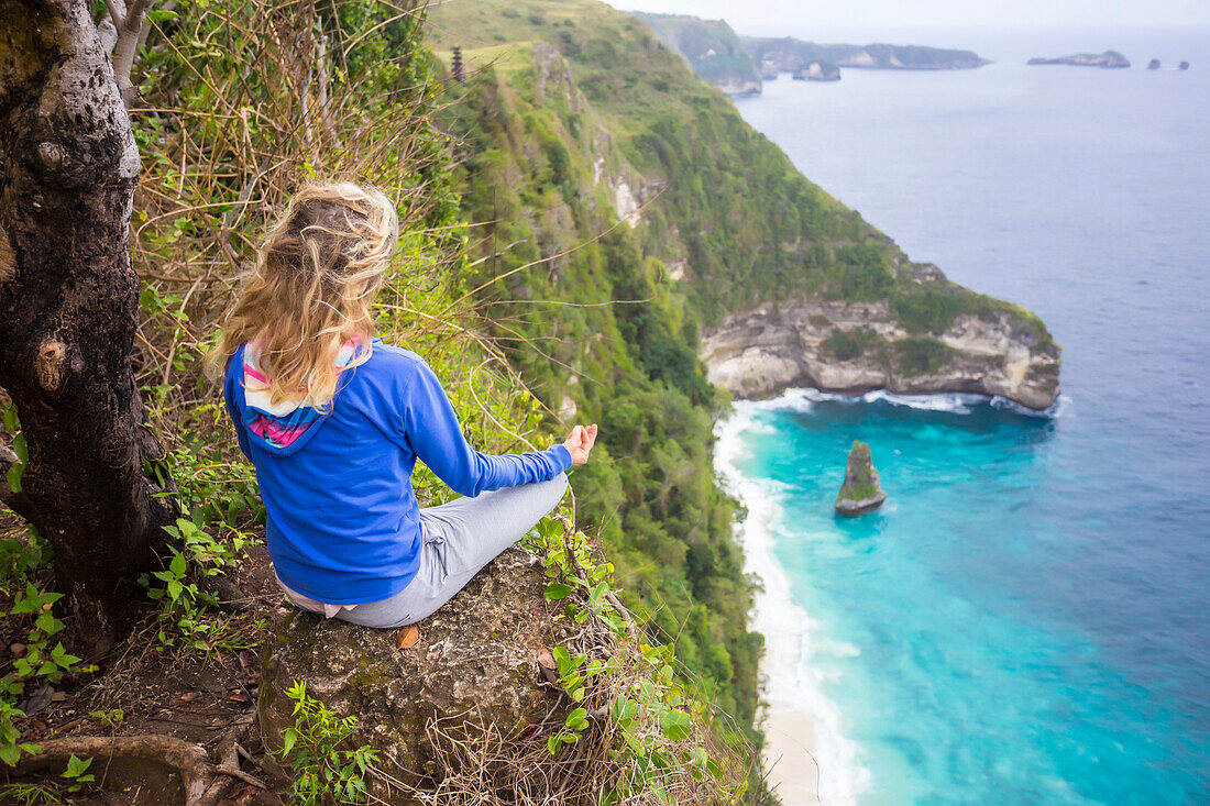 Blonde woman meditating on edge of coastline cliff, Bali, Indonesia
