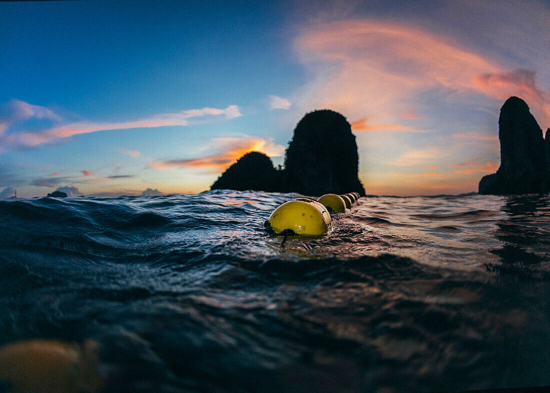 A line of buoys float in the water during sunset, Thailand