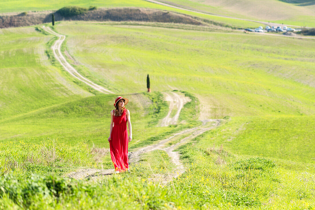 San Quirico d'Orcia, Orcia valley, Siena, Tuscany, Italy, A young woman in red dress walking along a country path near the cypresses of val d'orcia
