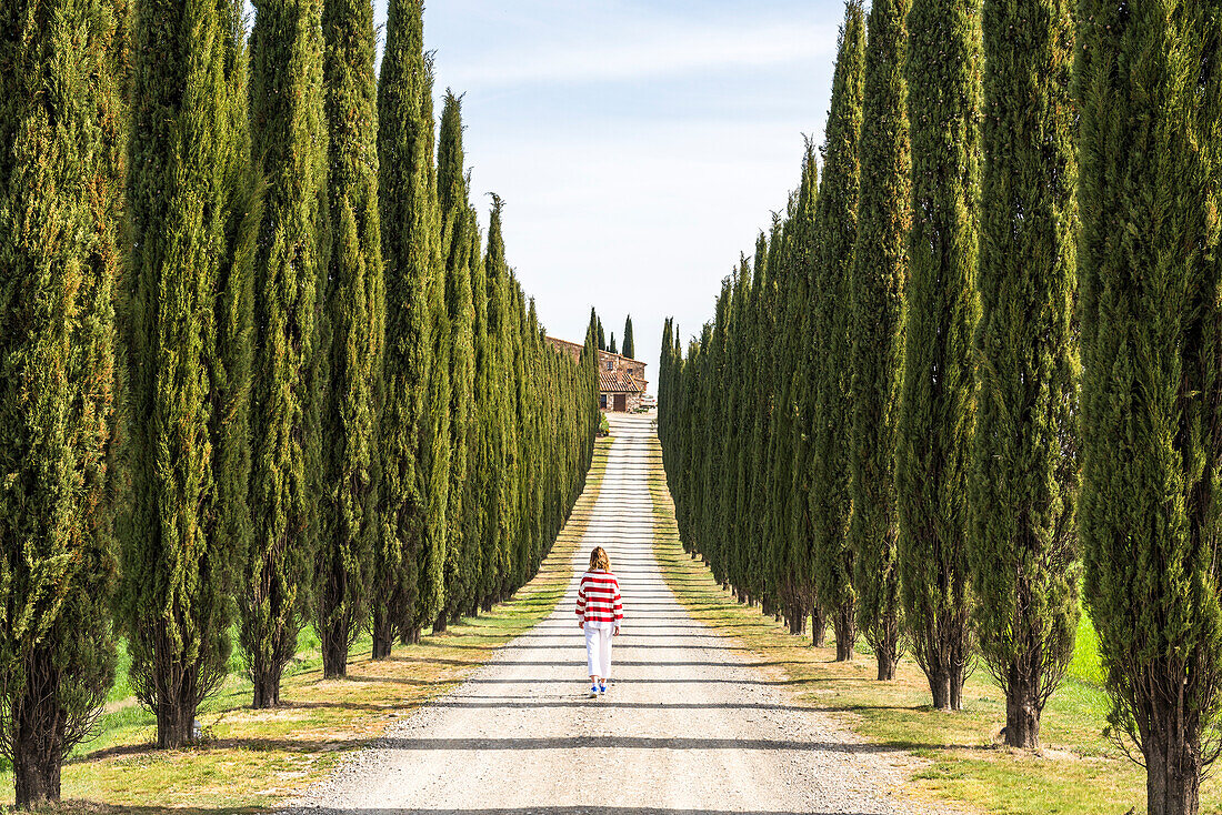 Castiglione d'Orcia, Orcia valley, Siena, Tuscany, Italy. A young woman in casual clothes is walking along a country road