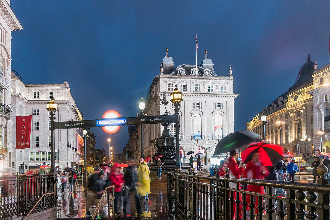 Menschen mit Sonnenschirmen am Piccadilly Circus in der Nacht, London, UK