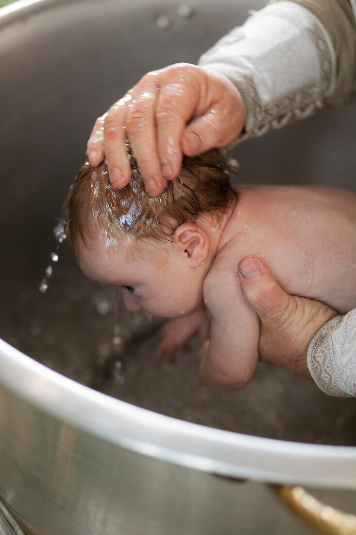 Priest baptizing baby girl with water