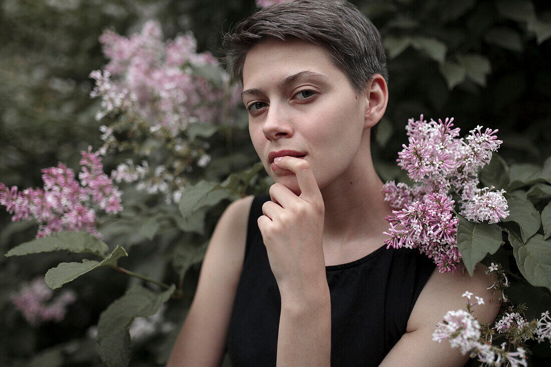 Neugierige kaukasische Frau in der Nähe eines blühenden Baums mit Finger auf der Lippe