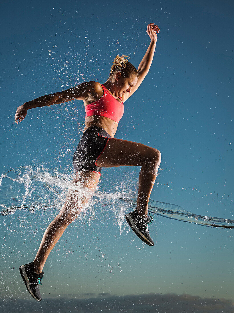 Water splashing on Caucasian woman running in sky