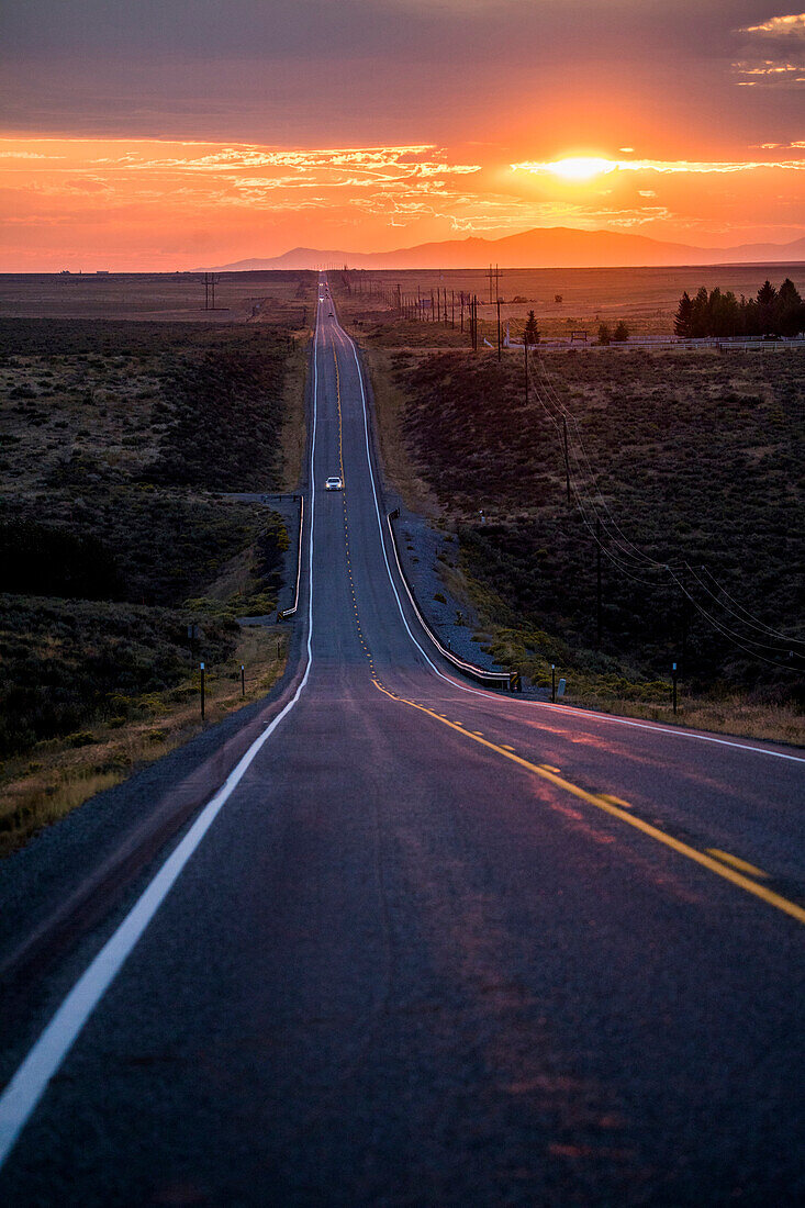 Cars driving on remote road at sunset
