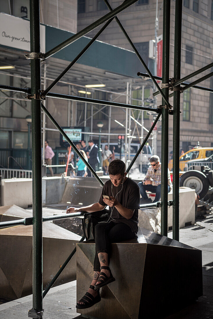 New Yorker sitzt rauchend vor einer Baustelle an der U-Bahn Station Wall Street und blickt auf sein Mobilfunk Telefon, Manhattan, New York City, Vereinigte Staaten von Amerika, USA, Nordamerika