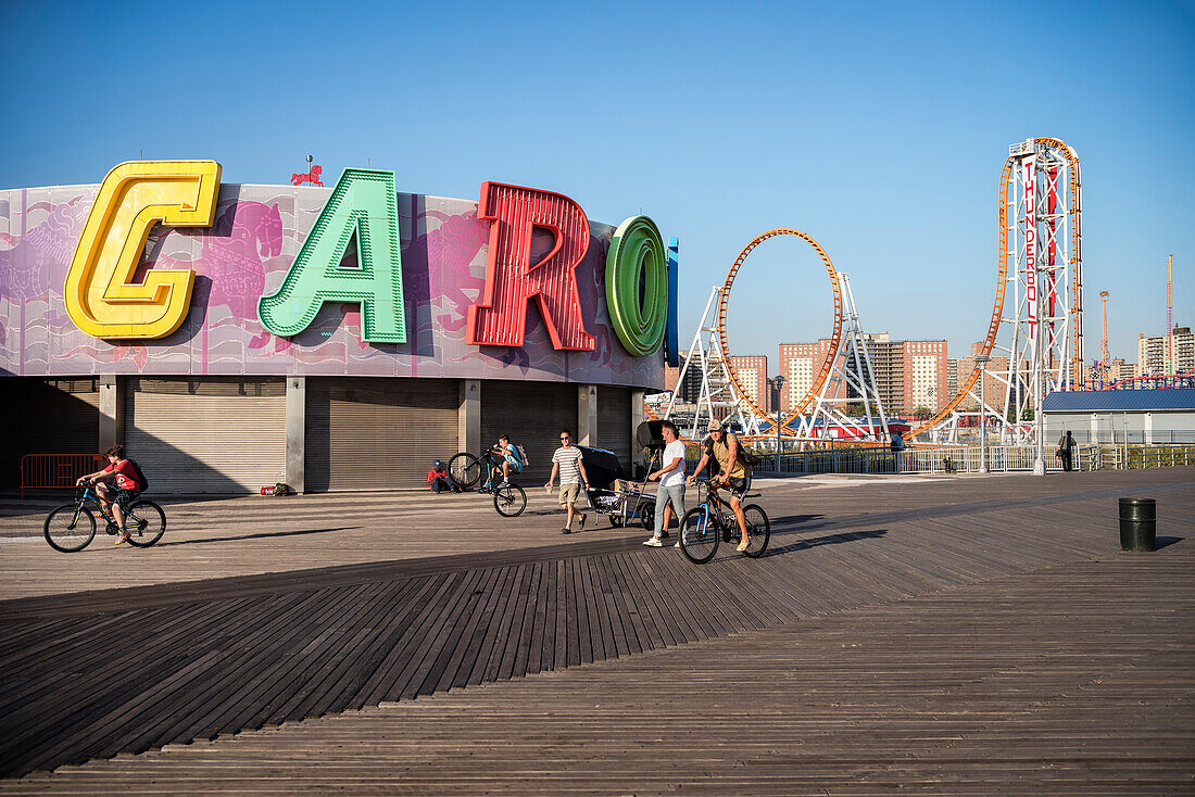 Cyclists and passing people in front of B & B Carousel at Luna Park Coney Island, Brooklyn, NYC, New York City, United States of America, USA, North America