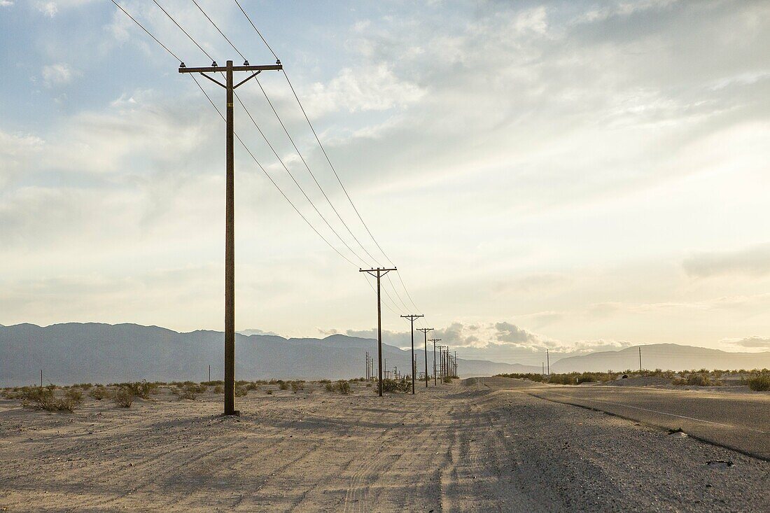 Drifting sand begins to cover roadway while power poles mark a border between desert and civilization.