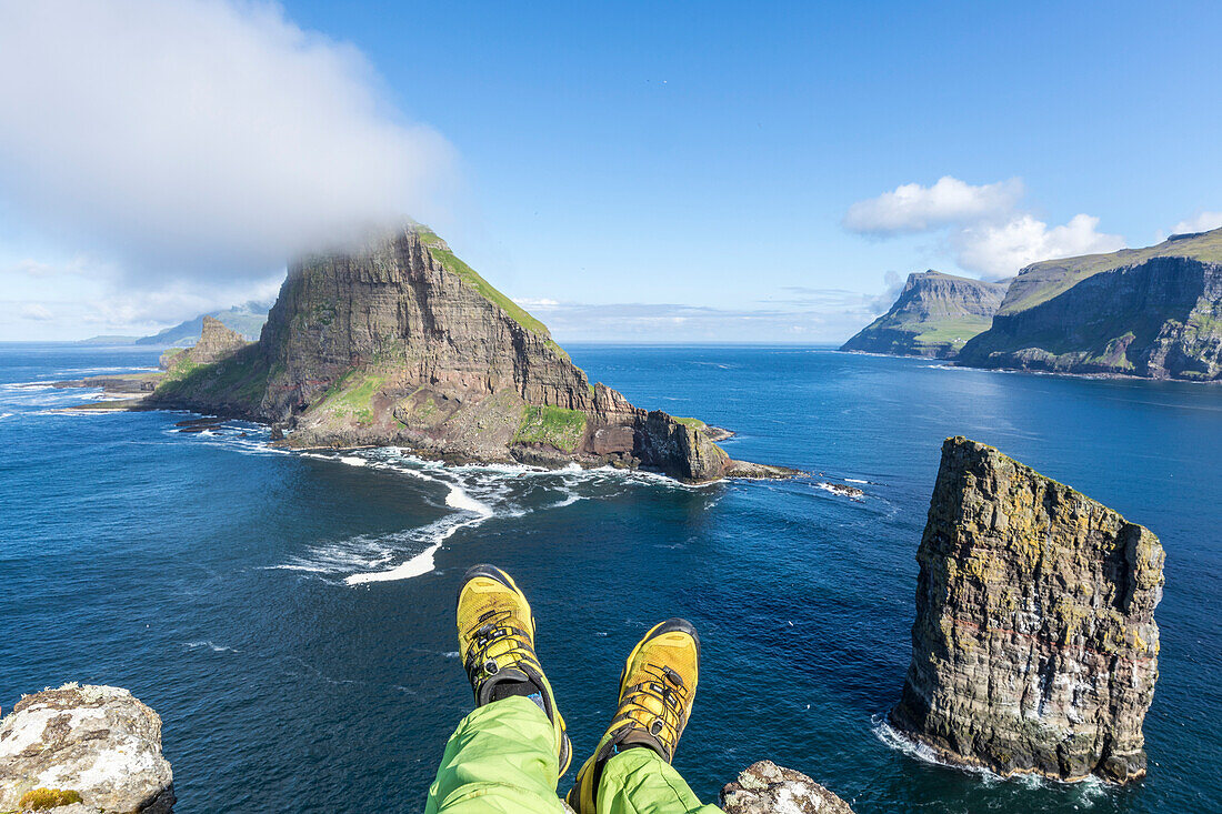 Man lays down on cliffs above the sea stacks of Drangarnir and Tindholmur islet, Vagar Island, Faroe Islands, Denmark, Europe