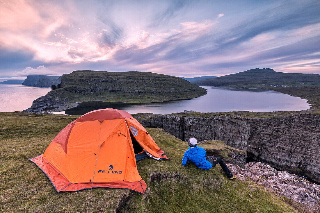 Camping tent and hiker on cliff above lake Sorvagsvatn at sunset, Vagar Island, Faroe Islands, Denmark, Europe