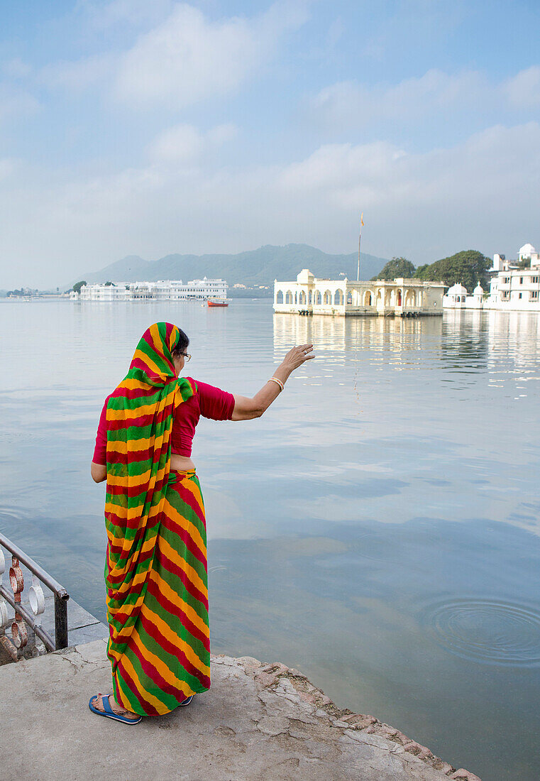 In the soft morning light, a Rajasthani woman in a sari looks over Lake Pichola, with the famous Lake Palace in the background, Udaipur, Rajasthan, India, Asia