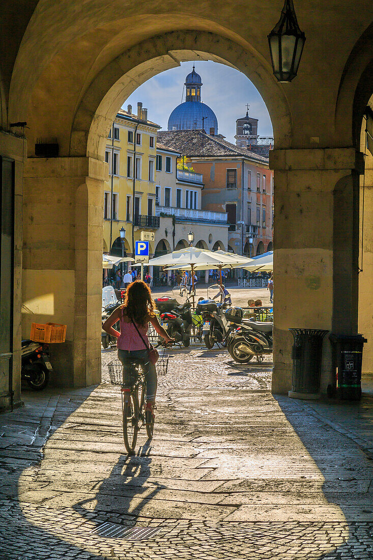 View of cyclist and Piazza delle Erbe through archways and dome of Padua Catherdal visible, Padua, Veneto, Italy, Europe