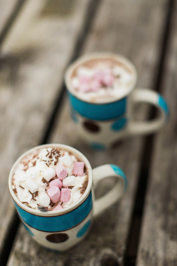 Close up of two mugs with hot chocolate and marshmallows lying on wooden surface, Scotland, UK