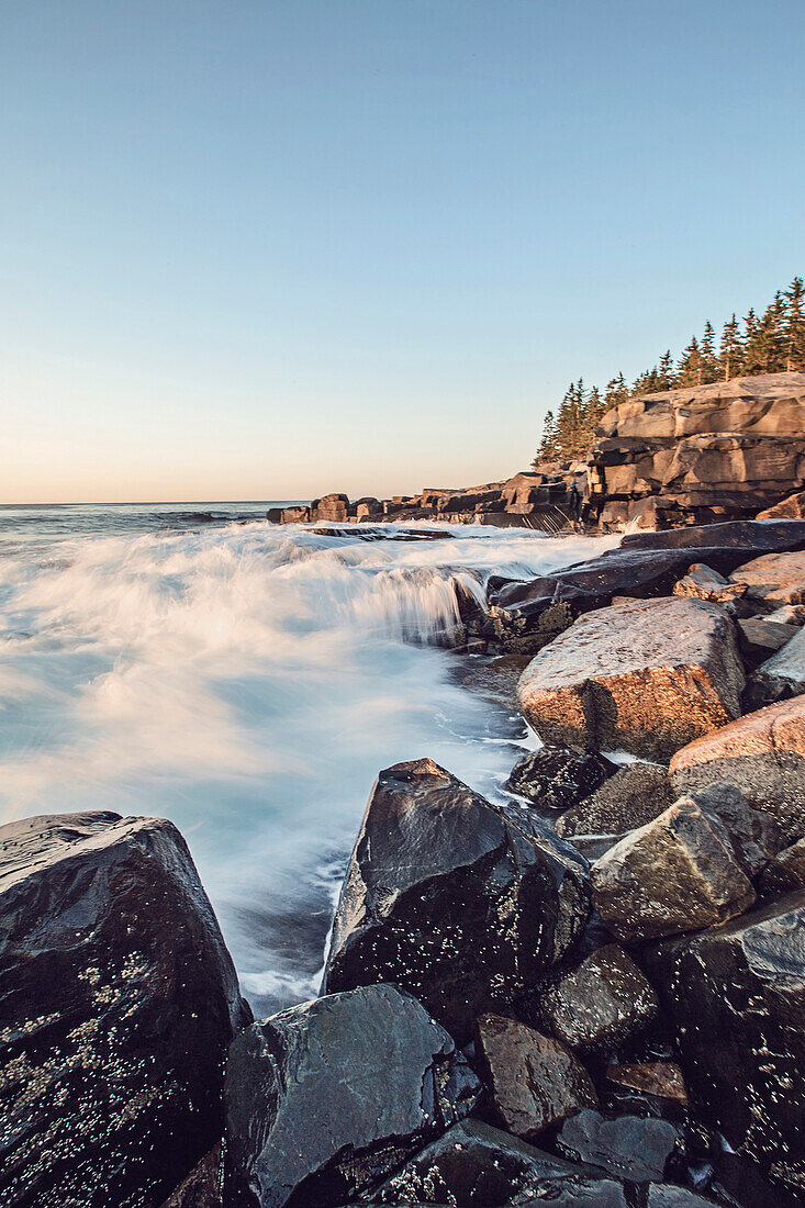 Waves crash along the shore at sunset in Maine's Acadia National Park.