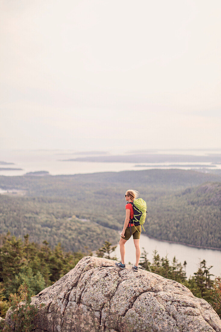 Female hiker standing and looking at view at summit of Pemetic Mountain, Acadia National Park, Maine, USA