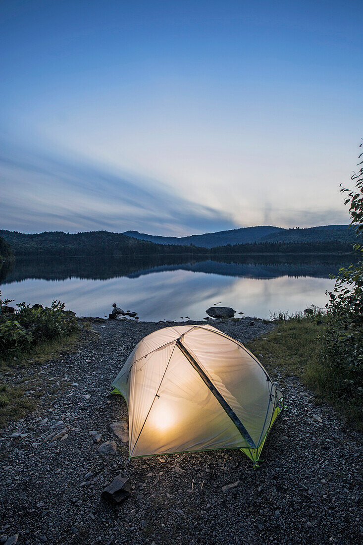 A tent glows at twilight on a lake in northern Maine.