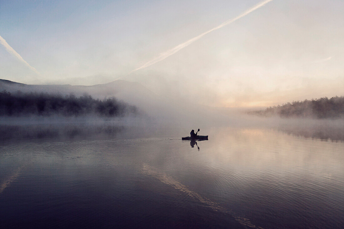 Young woman enjoys early morning paddle in kayak through mist on Daicey Pond in Maine's Baxter State Park, USA