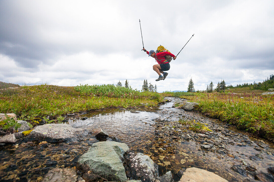 Side view of man jumping across small stream, Merritt, British Columbia, Canada