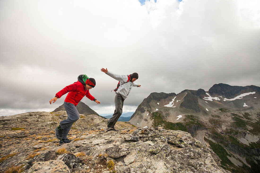 Two hikers battling strong wind on rocky ridge, Merritt, British Columbia, Canada