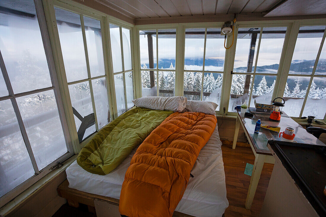 Sleeping bags on bed inside Pickett Butte Fire Lookout with snowy landscape outside, Tiller, Oregon, USA