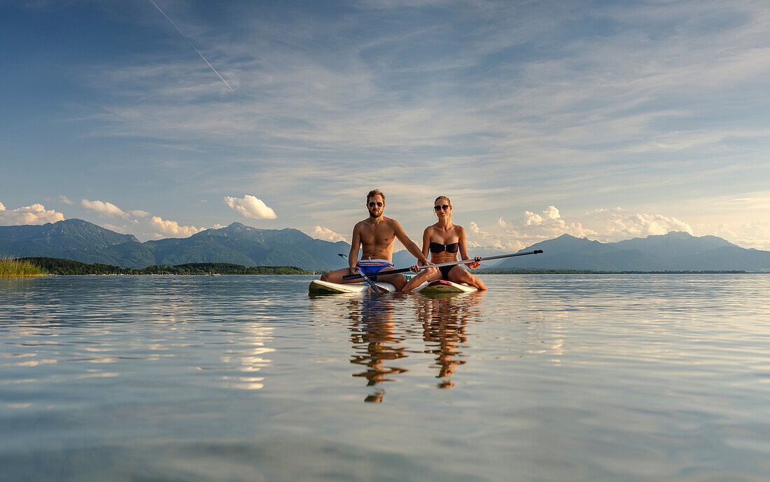 A young couple on their SUP boards on the Chiemsee, in the background the Chiemgau Alps, Chieming, Upper Bavaria, Germany