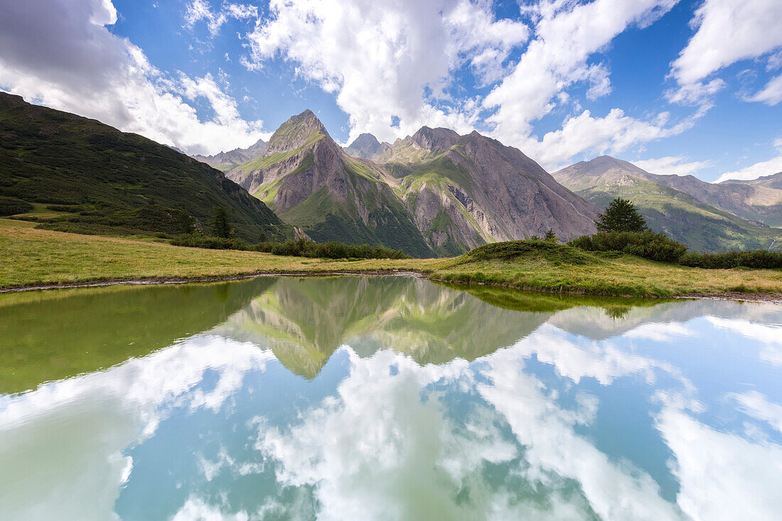 View of Punta di Morasco, Corno di Ban and Punta della Sabbia reflected in a small carsic lake over Riale. Riale hamlet, Formazza, Valle Formazza, Verbano Cusio Ossola, Piedmont, Italy.